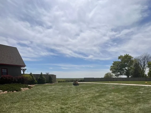A wide, freshly cut lawn with mowing stripes running to a treeline, beside a barn-style home.